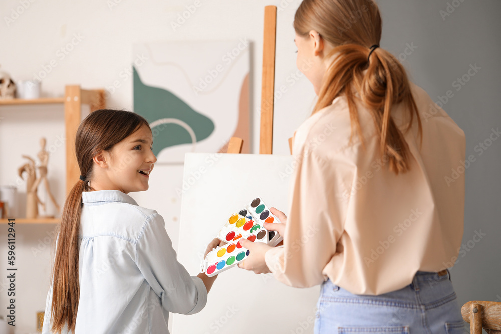 Drawing teacher giving private art lesson to little girl near easel in workshop