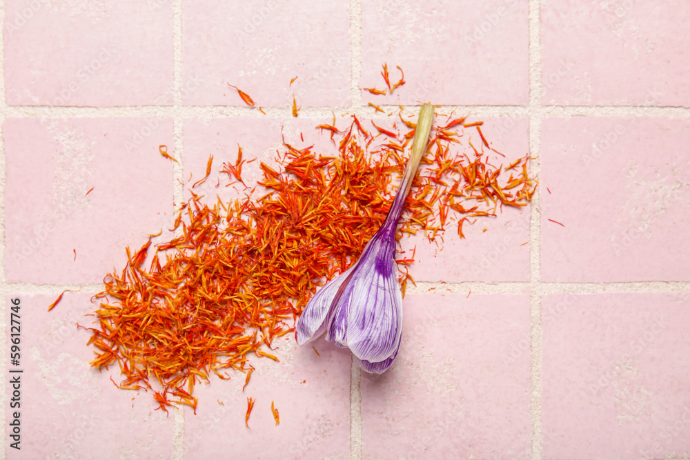 Heap of dried saffron threads and crocus flower on pink tiled table