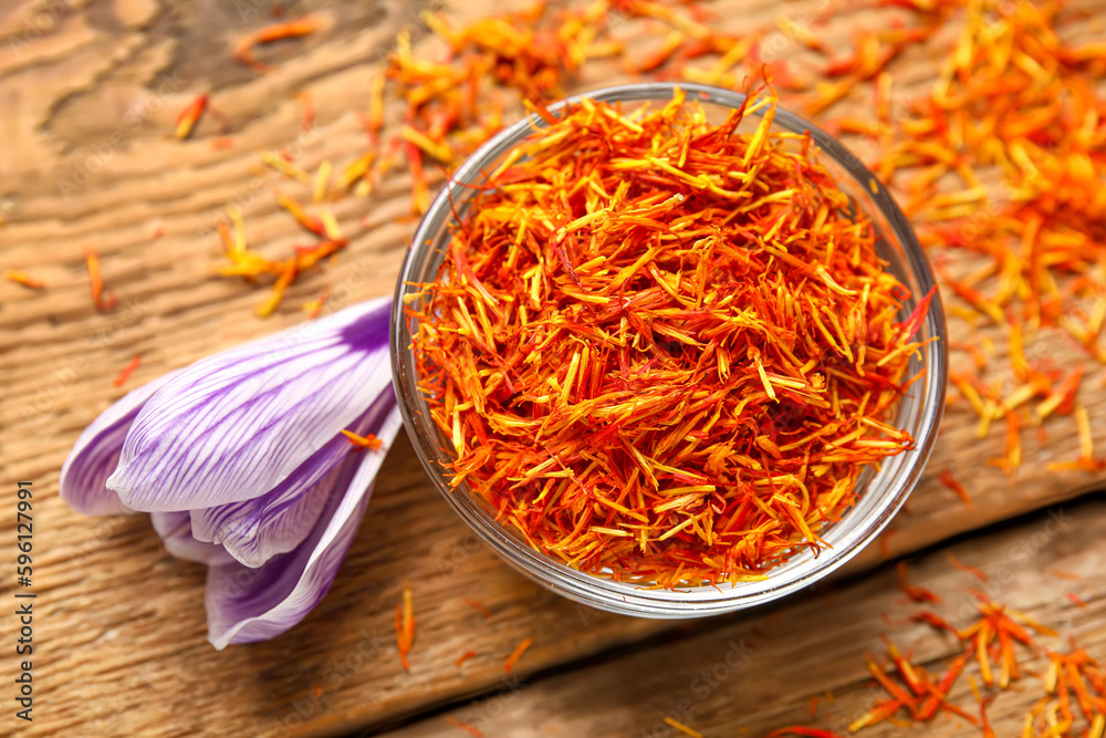 Bowl of dried saffron threads with crocus flower on wooden table