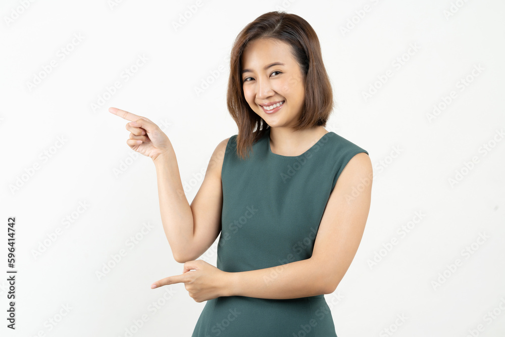 Young smiling Asian woman pointing finger sideways to copy space in pink color background.