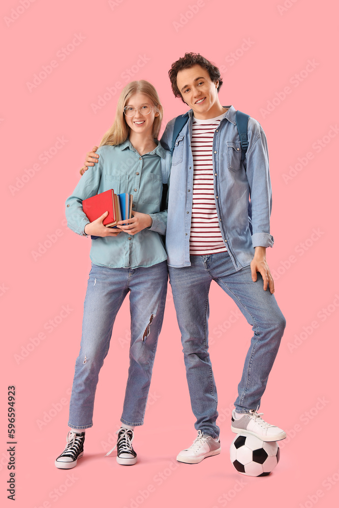 Teenage couple with books and soccer ball on pink background