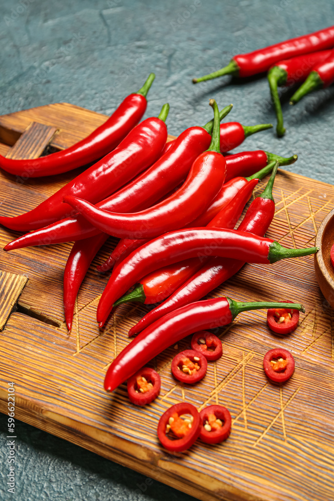 Wooden board with fresh chili peppers on dark background