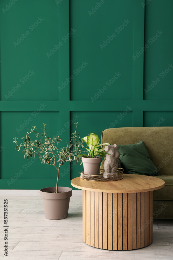 Cozy sofa, houseplants and coffee table with woman figurine near green wall