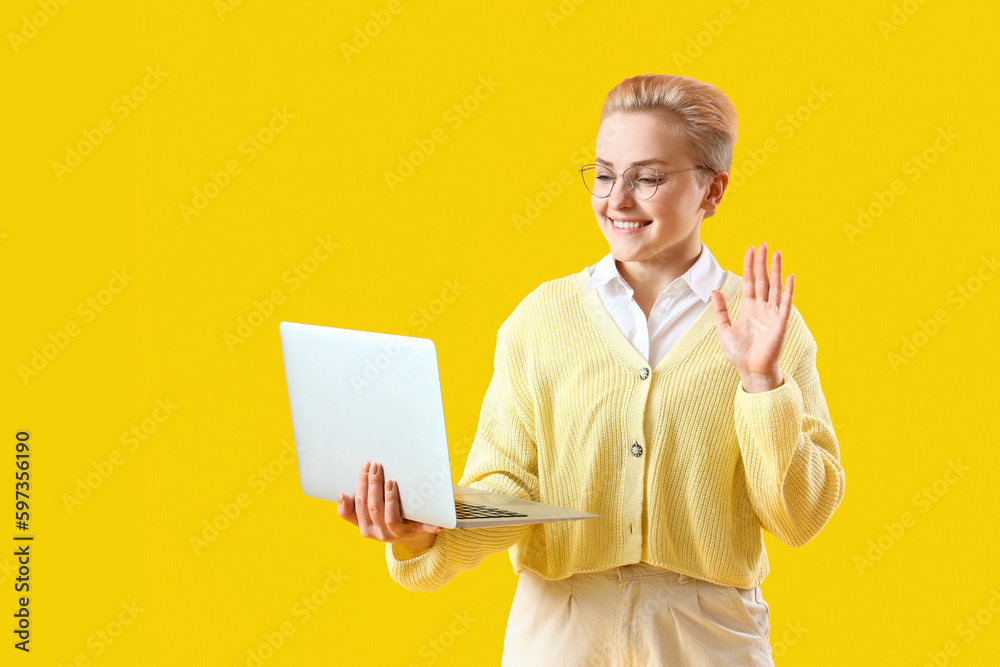 Female student with laptop video chatting on yellow background