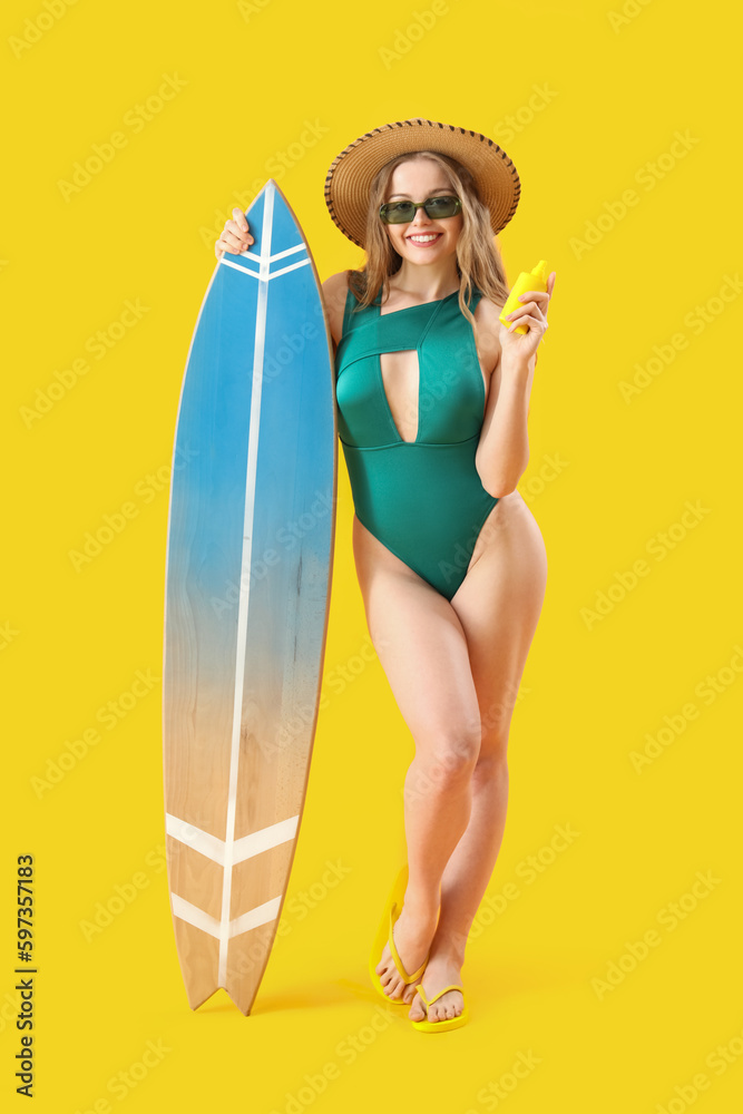 Beautiful young woman with sunscreen cream and surfboard on yellow background