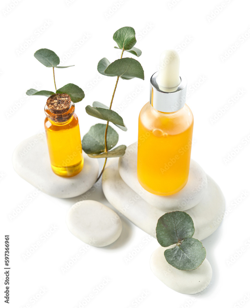 Bottles with cosmetic oil, eucalyptus branch and stones on white background