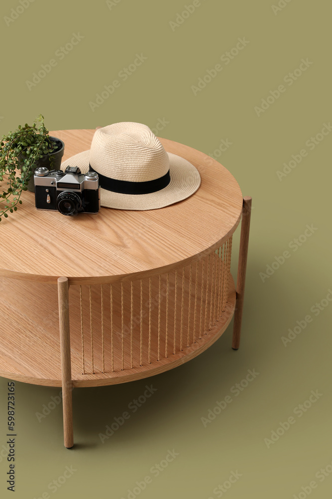 Wooden coffee table with camera, hat and houseplant on green background