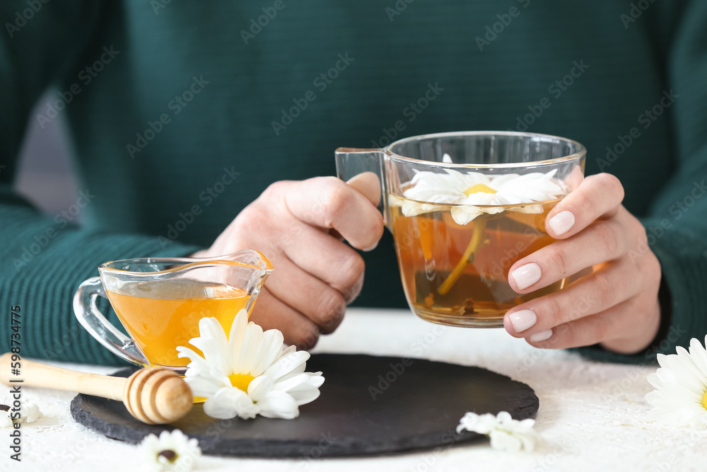 Female hands with cup of tea, honey and beautiful chrysanthemums on white table
