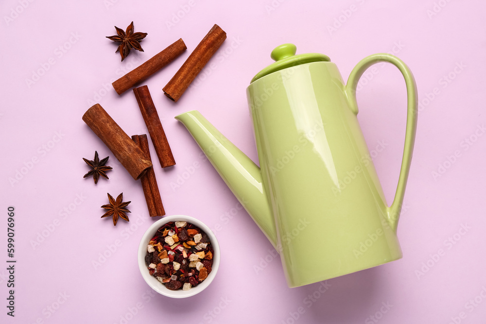 Ceramic teapot with spices and dried fruits on lilac background