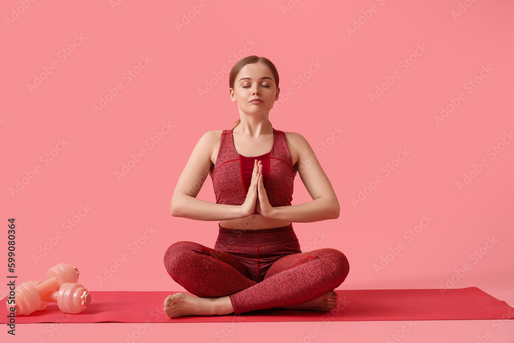 Sporty young woman meditating on pink background