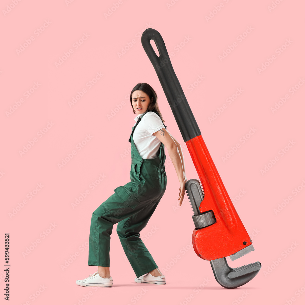 Worried female plumber with big pipe wrench on pink background