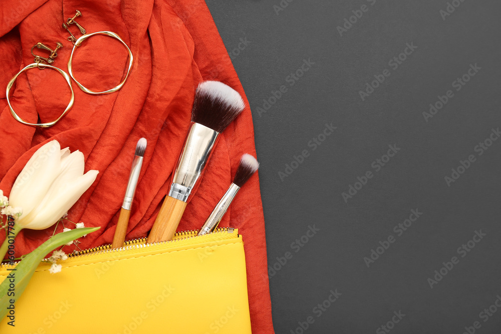 Composition with stylish earrings, makeup brushes and flowers on dark background