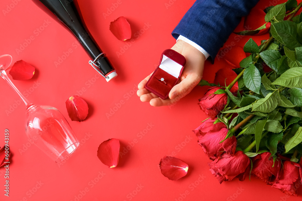 Man with engagement ring, bottle of wine, glass and roses on red background