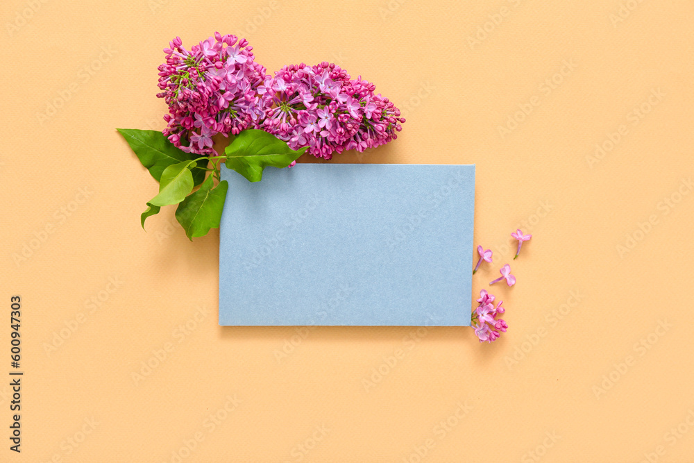 Blue blank card and beautiful lilac flowers on pale orange background