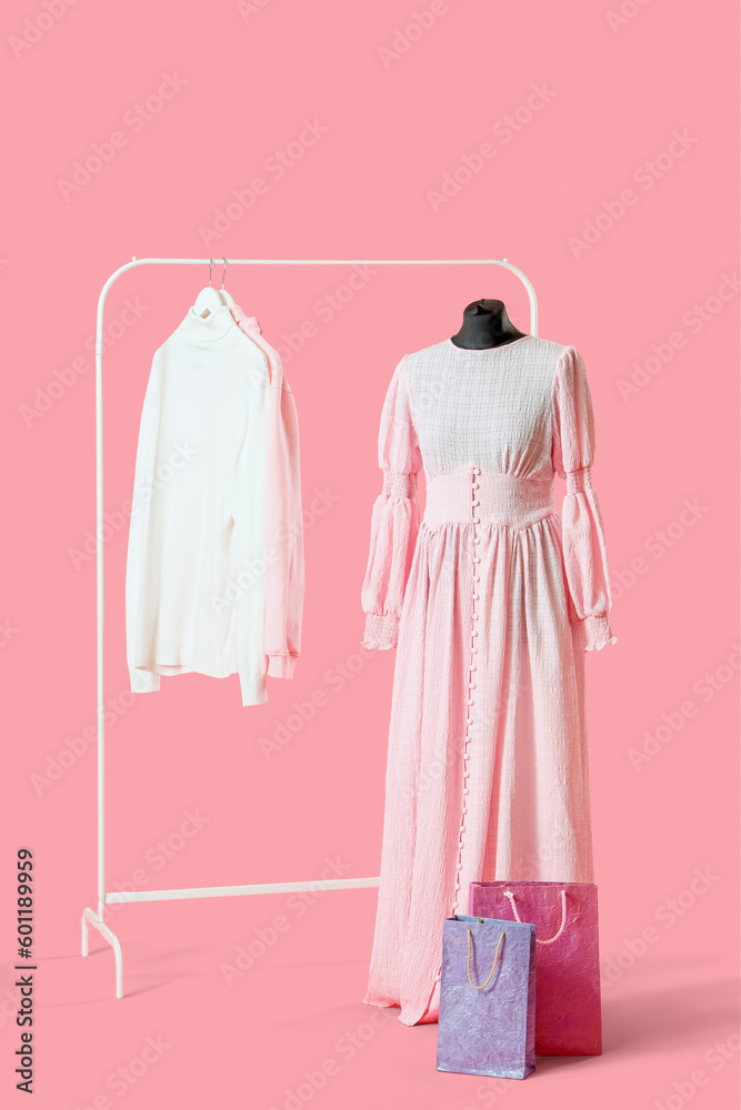 Mannequin with rack, stylish clothes and shopping bags on pink background