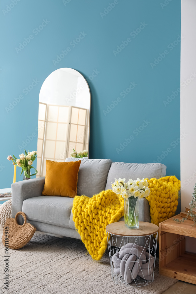 Interior of stylish living room with cozy grey sofa and mirror near blue wall