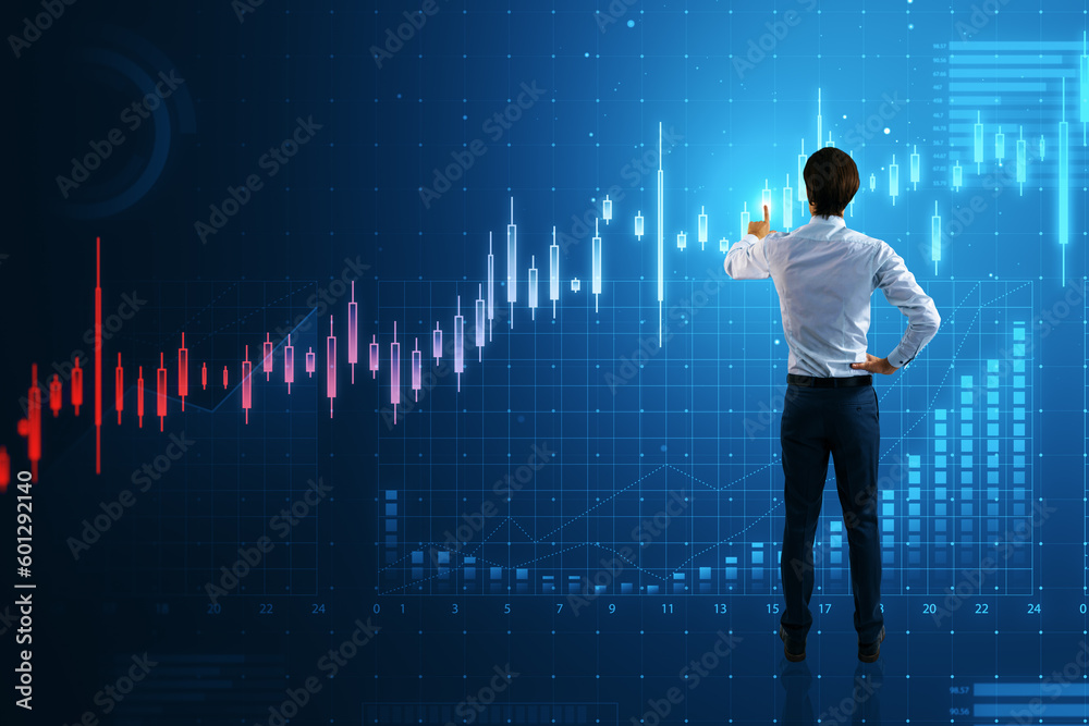 Back view of young businessman using abstract glowing candlestick business chart on blue background.