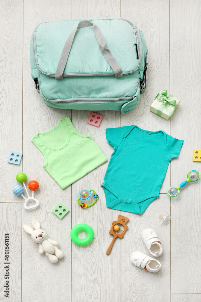 Stylish bag with clothes and toys for baby on light wooden background