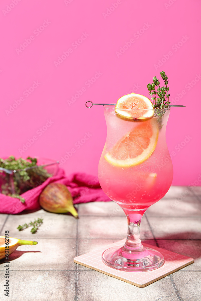Fresh summer cocktail with fig, grapefruit and thyme on tile table near pink wall