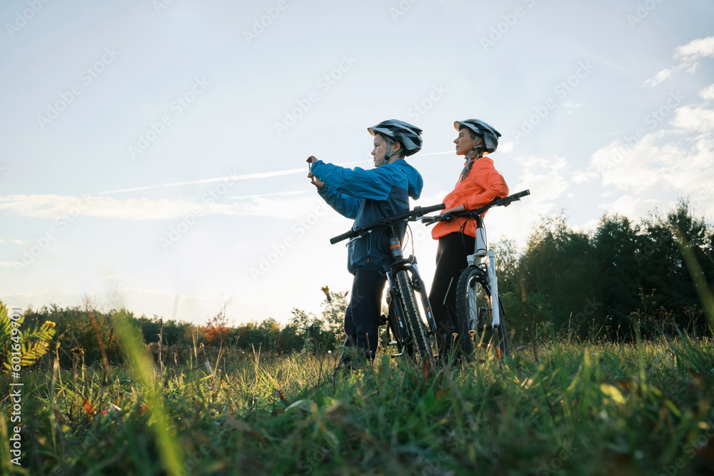 Mother and son ride a bike. Happy cute boy in helmet takes a photo on a smartphone. Family to riding