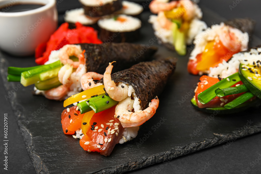 Slate board with tasty sushi cones on dark background, closeup