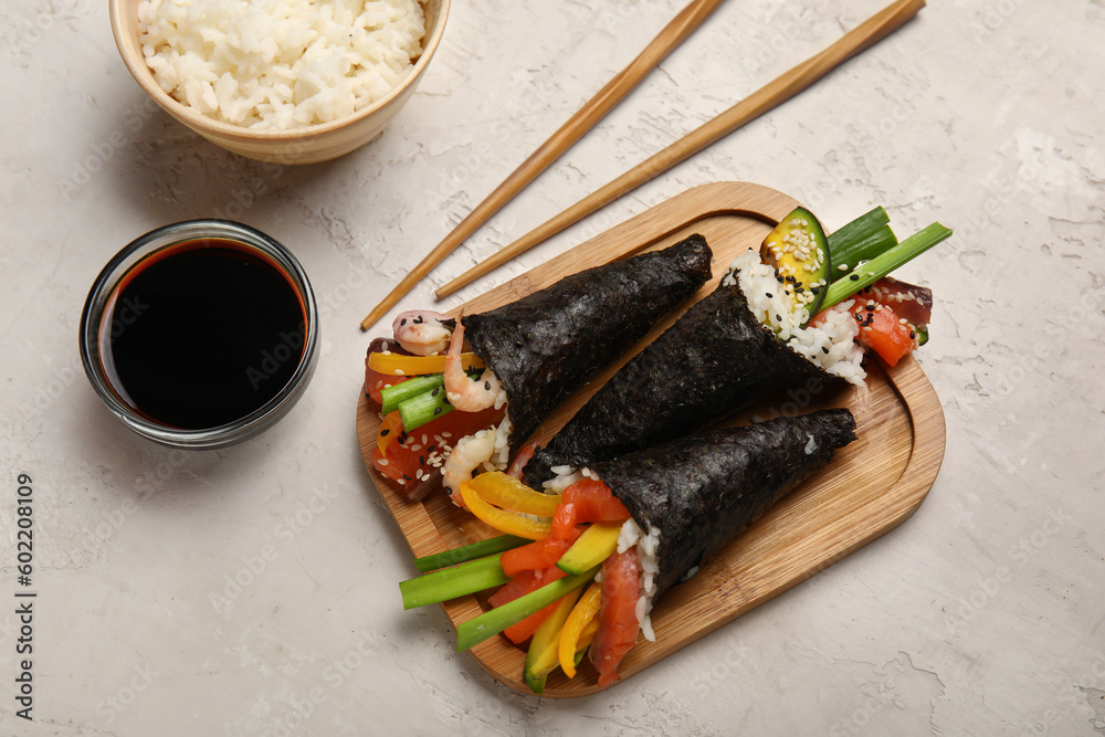 Wooden board with tasty sushi cones, soy sauce, boiled rice and chopsticks on light background
