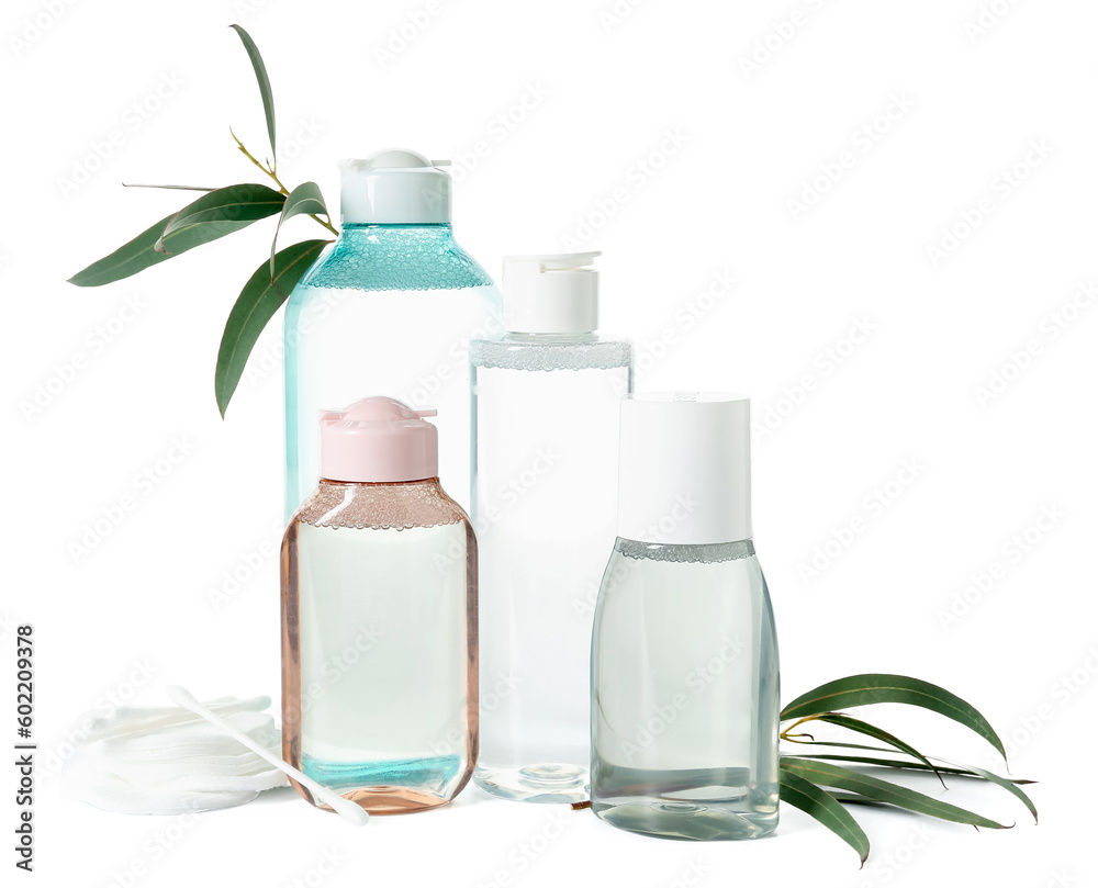 Bottles of micellar water, cotton buds, pads and plant branches on white background