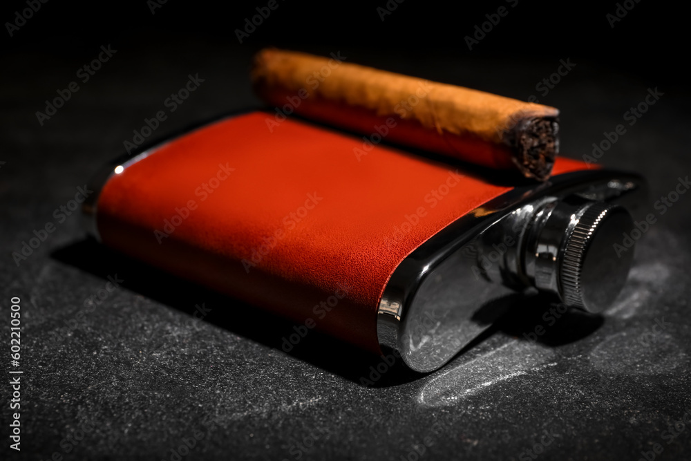 New hip flask with cigar on dark background