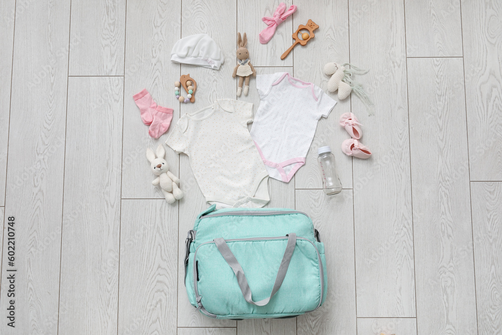 Stylish bag with clothes and toys for baby on light wooden background
