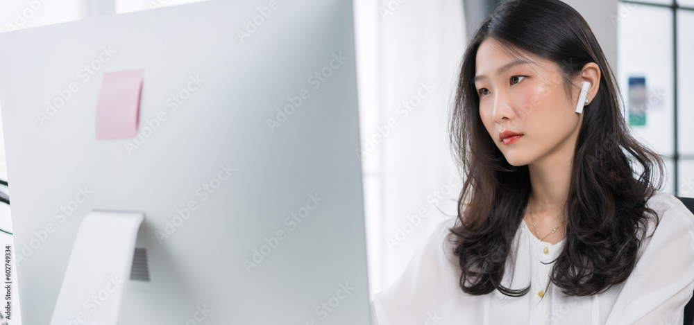 Young asian girl working at a home with a computer and wearing earphones