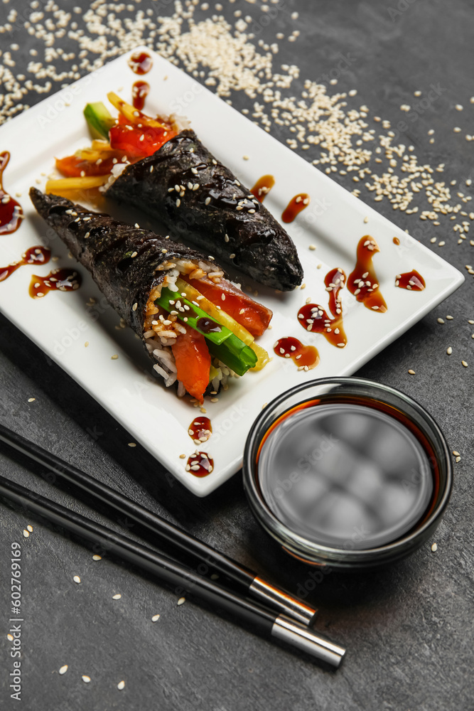 Plate with tasty sushi cones, soy sauce and sesame seeds on dark background, closeup