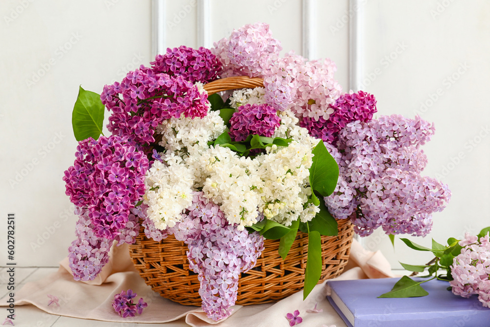 Wicker basket with beautiful fragrant lilac flowers near white wooden wall