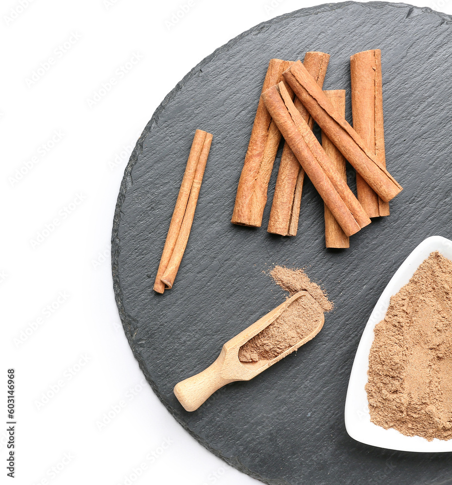 Slate board with cinnamon powder and sticks on white background, closeup