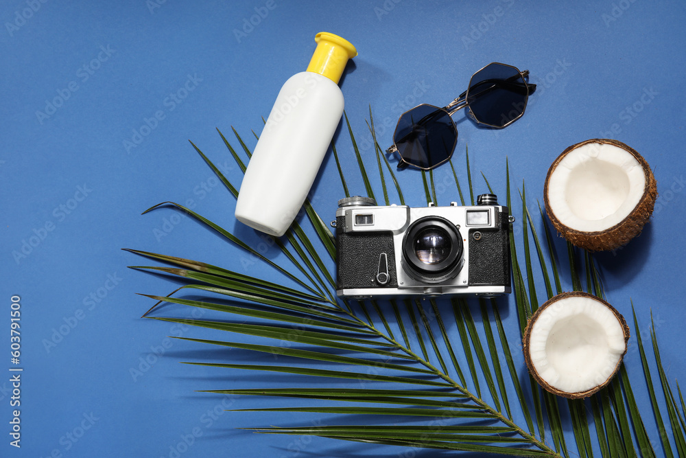 Palm leaf with coconut, photo camera, sunglasses and sunscreen cream on blue background