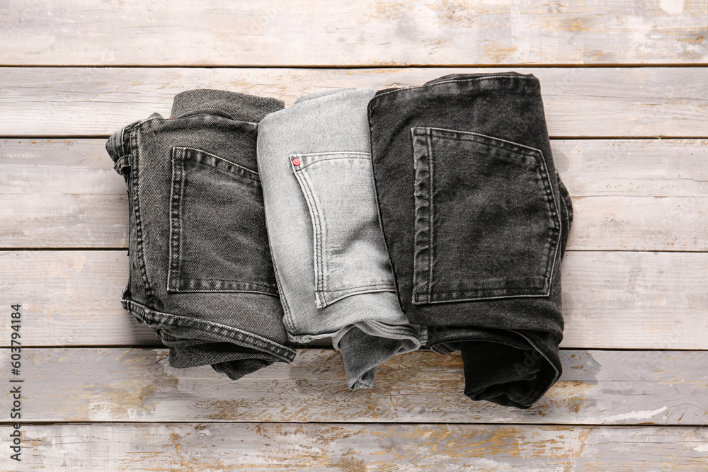 Different rolled denim jeans on wooden background