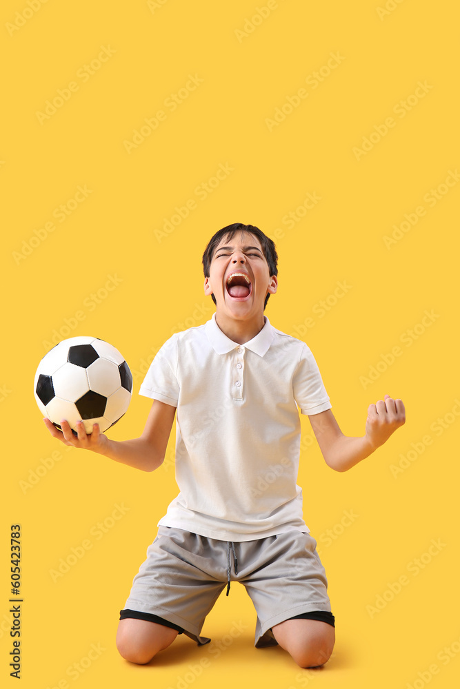 Happy little boy with soccer ball on yellow background