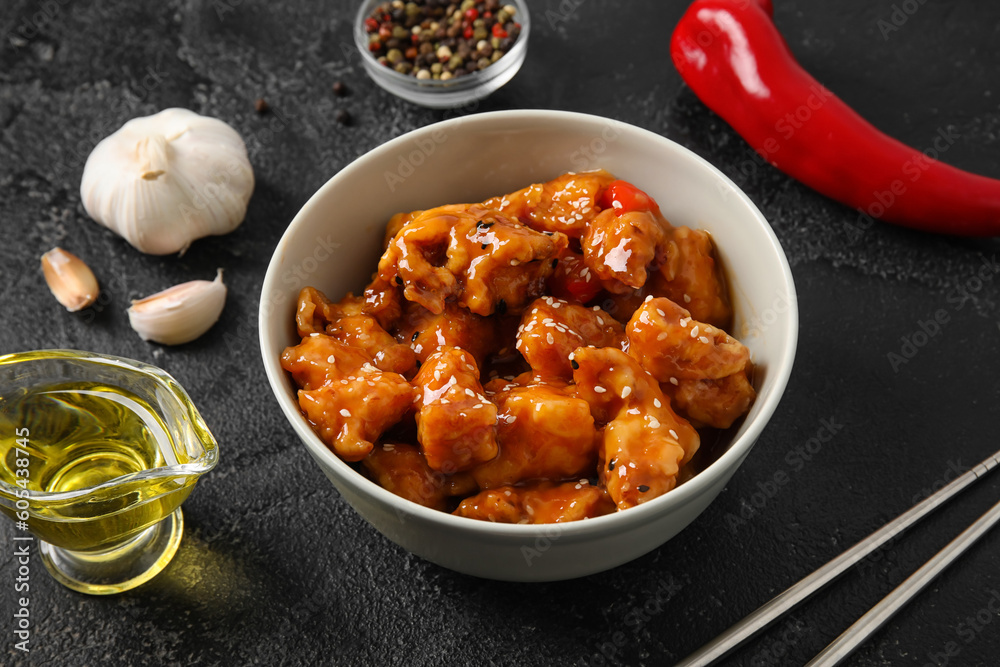 Tasty sweet and sour chicken in bowl with spices on dark background, closeup