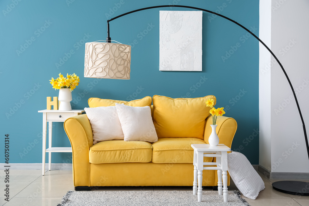 Cozy yellow sofa with cushions and blooming narcissus flowers on table in living room