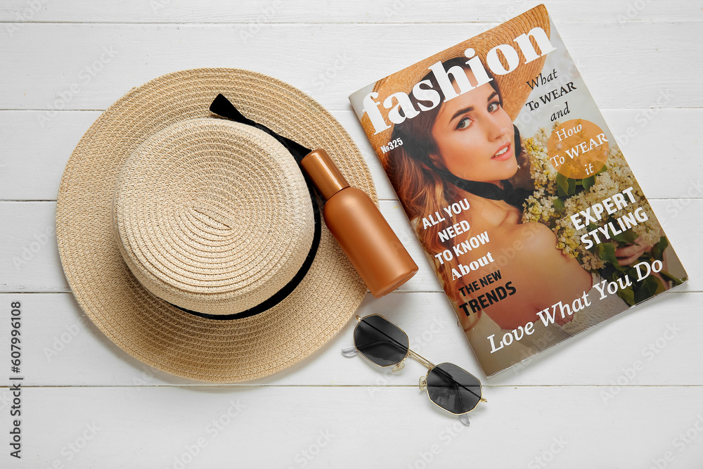 Bottle of sunscreen cream, sunglasses, magazine and wicker hat on light wooden background