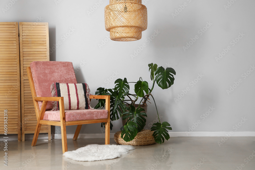 Cozy pink armchair with cushion, houseplant and folding screen near grey wall