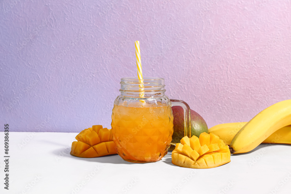 Mason jar of fresh mango smoothie and bananas on color background