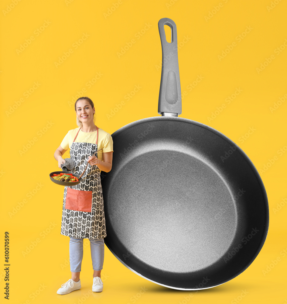 Housewife in apron and big frying pan on yellow background