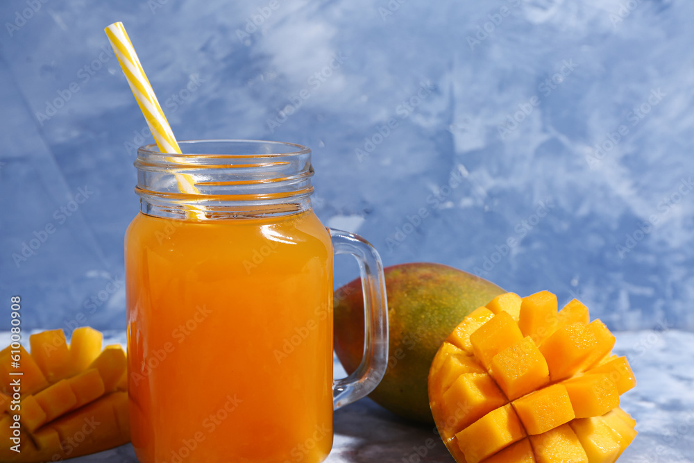 Mason jar of fresh mango smoothie on blue background, closeup