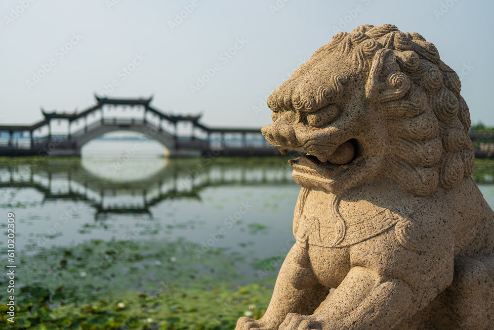 Chinese traditional style stone lion with wooden bridge and lotus pool in background