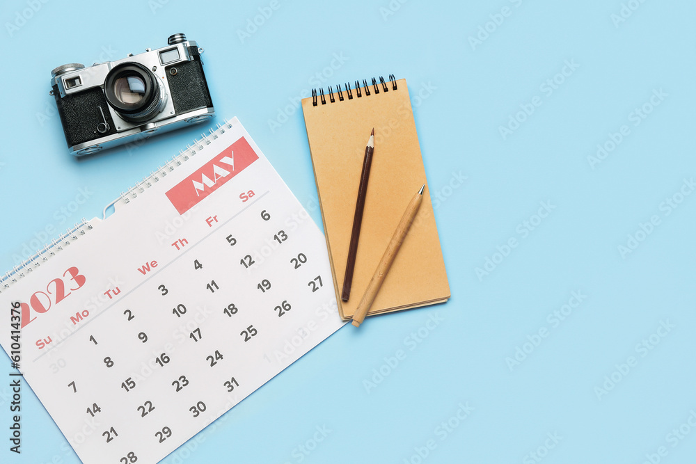 Composition with calendar, photo camera, notebook and pencils on blue background