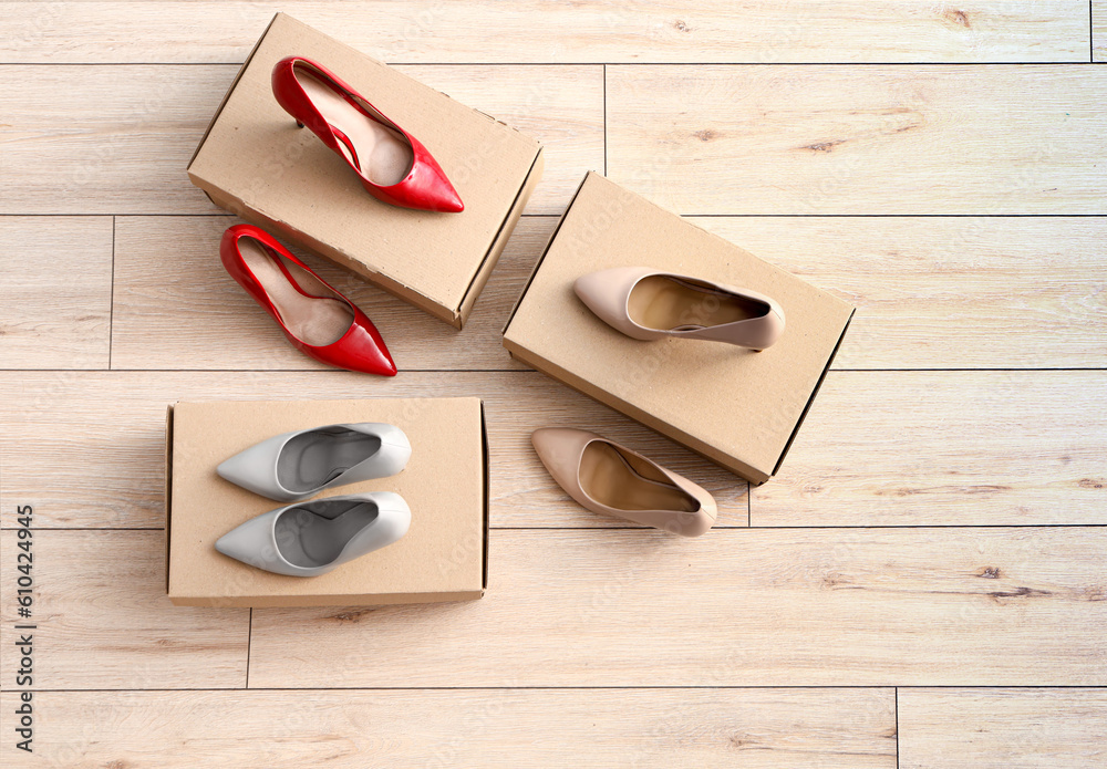 Cardboard boxes with high-heeled shoes on light wooden background