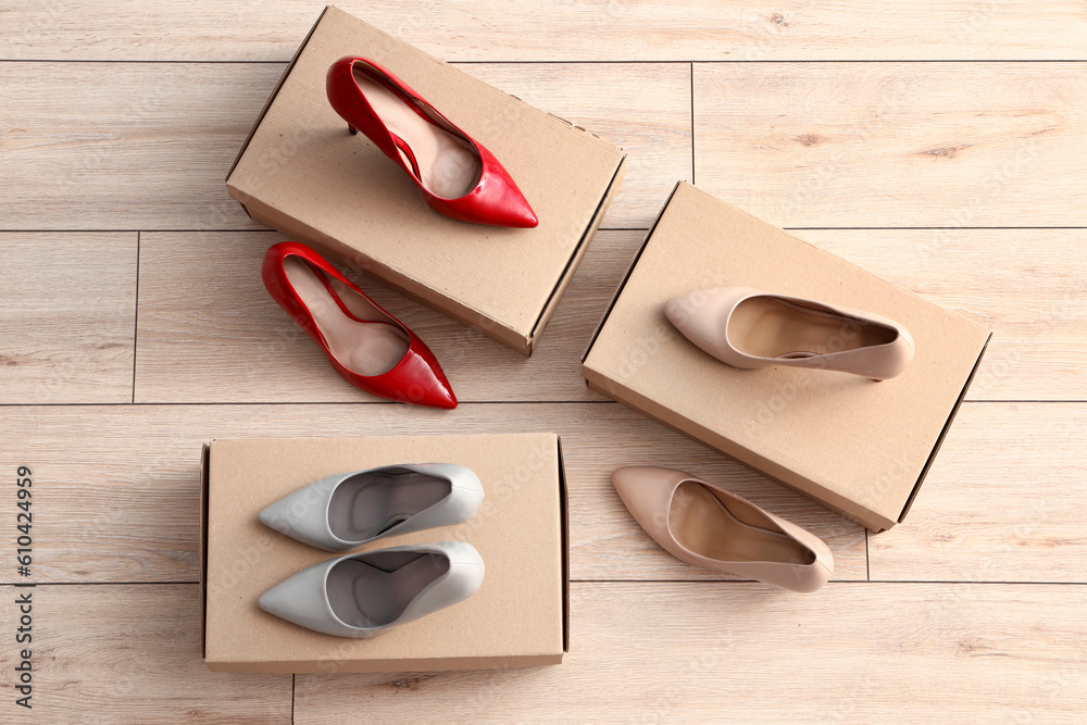 Cardboard boxes with high-heeled shoes on light wooden background