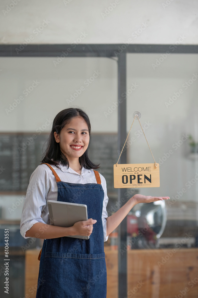 A beautiful and friendly young Asian female waitress in an apron stands at the coffee shop entrance 
