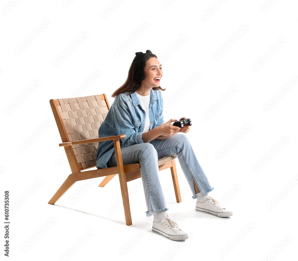 Young woman with headphones playing video game in wooden armchair on white background