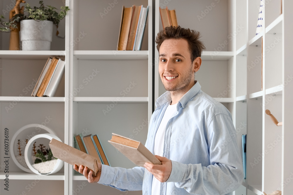 Young man with books near shelving unit at home